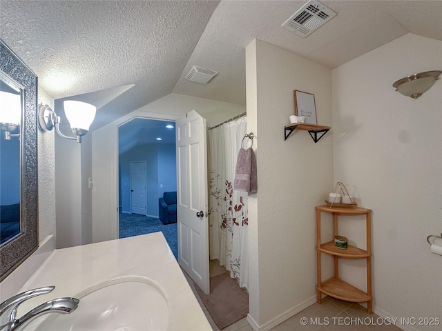 bathroom featuring vanity, lofted ceiling, visible vents, and a textured ceiling