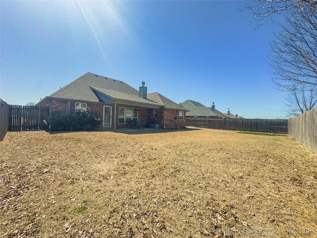 rear view of property with a yard, a fenced backyard, brick siding, and a chimney