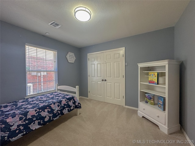 bedroom featuring visible vents, baseboards, light colored carpet, a closet, and a textured ceiling