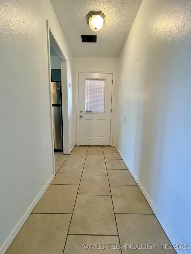 hallway featuring light tile patterned flooring, baseboards, visible vents, and a textured ceiling