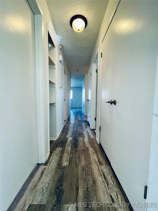 corridor with a textured ceiling and dark wood-type flooring