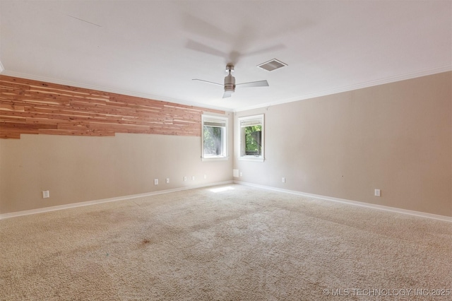 carpeted spare room with baseboards, a ceiling fan, visible vents, and ornamental molding