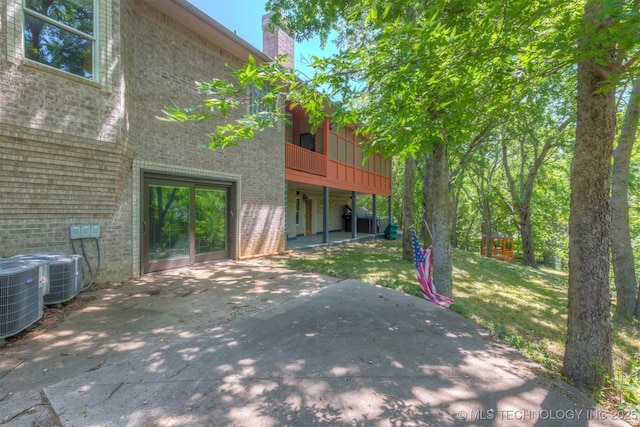 rear view of house with central air condition unit, a patio, a lawn, and brick siding