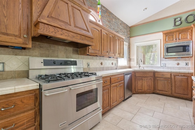 kitchen featuring tile countertops, premium range hood, lofted ceiling, a sink, and stainless steel appliances