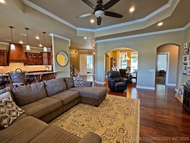 living room featuring arched walkways, dark wood-style floors, a raised ceiling, and a ceiling fan