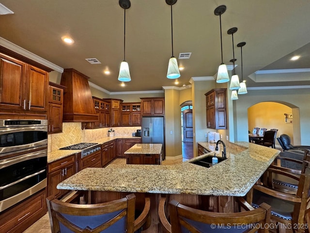 kitchen with a spacious island, custom range hood, arched walkways, stainless steel appliances, and a sink