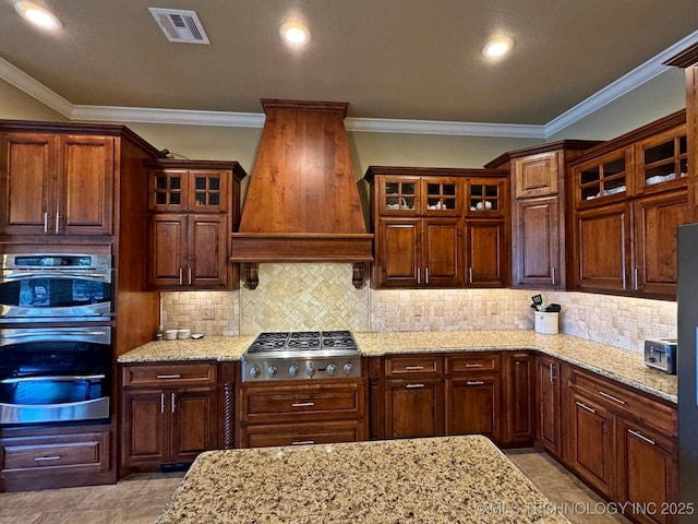 kitchen with tasteful backsplash, visible vents, light stone countertops, premium range hood, and appliances with stainless steel finishes