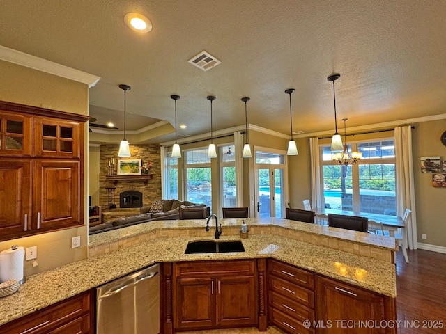 kitchen with visible vents, a sink, stainless steel dishwasher, a stone fireplace, and crown molding