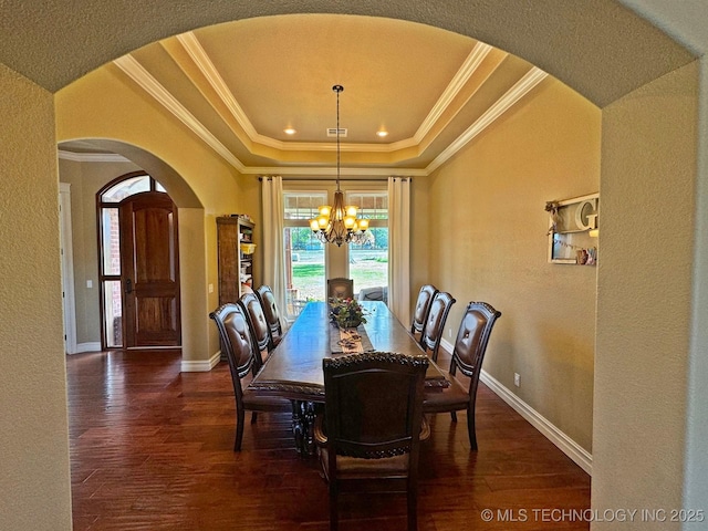 dining room with a notable chandelier, dark wood-type flooring, a tray ceiling, arched walkways, and crown molding