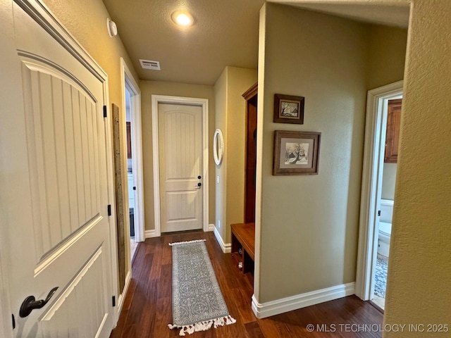 entryway featuring dark wood finished floors, baseboards, visible vents, and a textured wall
