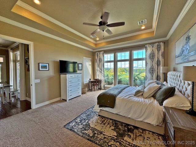 carpeted bedroom featuring a tray ceiling, baseboards, visible vents, and crown molding