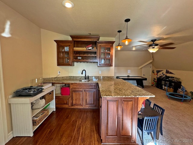 kitchen featuring a ceiling fan, a sink, a peninsula, brown cabinetry, and lofted ceiling