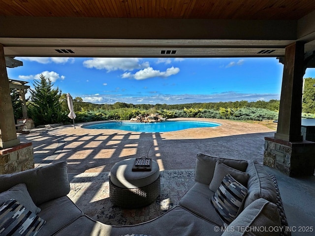 pool with a patio area and a wooded view