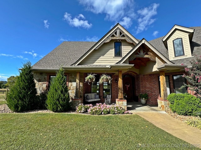 view of front of home featuring stone siding, brick siding, roof with shingles, and a front yard