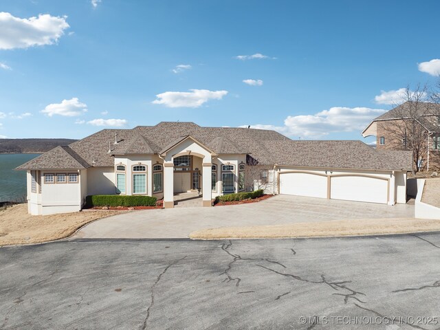 view of front of home with stucco siding, an attached garage, concrete driveway, and a water view