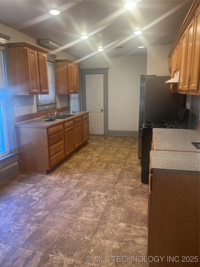 kitchen featuring ventilation hood, brown cabinetry, baseboards, a sink, and black range with gas cooktop