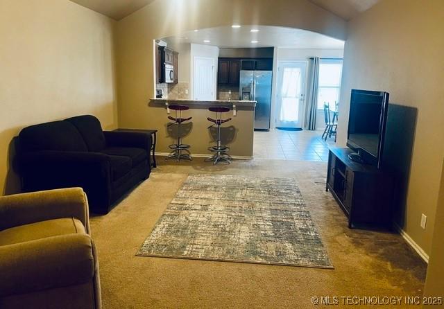 living room featuring vaulted ceiling, light tile patterned flooring, and baseboards