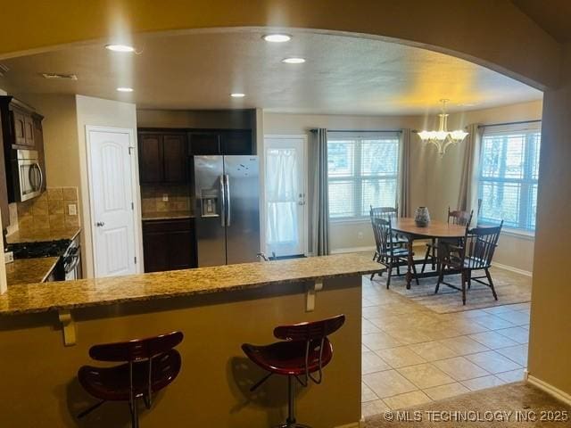 kitchen with a breakfast bar, a chandelier, stainless steel appliances, and decorative backsplash