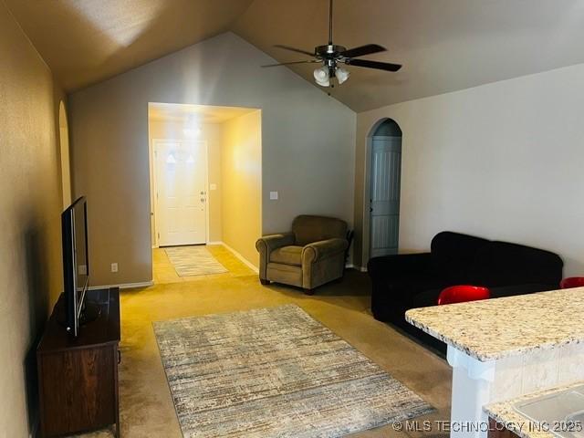 living room with baseboards, lofted ceiling, arched walkways, ceiling fan, and light colored carpet