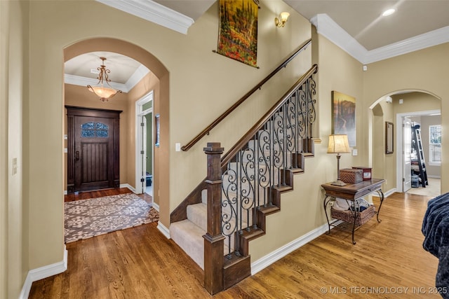 entrance foyer featuring baseboards, ornamental molding, wood finished floors, arched walkways, and stairway