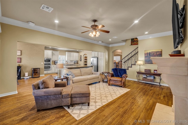 living room featuring ornamental molding, visible vents, a ceiling fan, and arched walkways