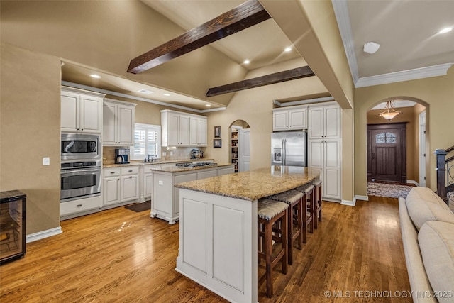 kitchen with ornamental molding, a kitchen island, arched walkways, beamed ceiling, and appliances with stainless steel finishes