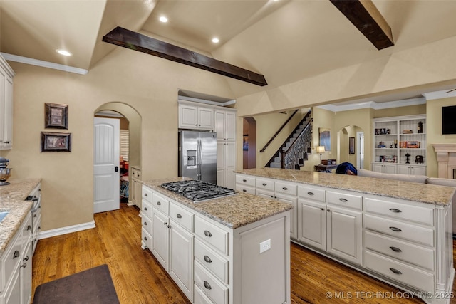 kitchen featuring a kitchen island, arched walkways, lofted ceiling with beams, white cabinets, and appliances with stainless steel finishes