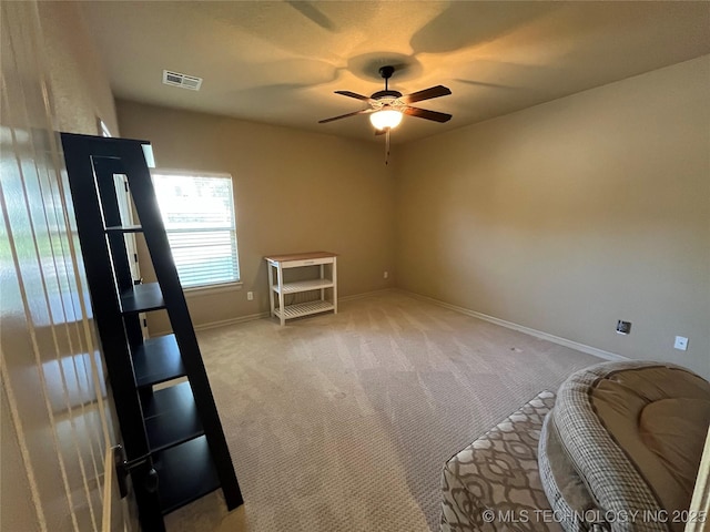 interior space featuring baseboards, a ceiling fan, visible vents, and light colored carpet
