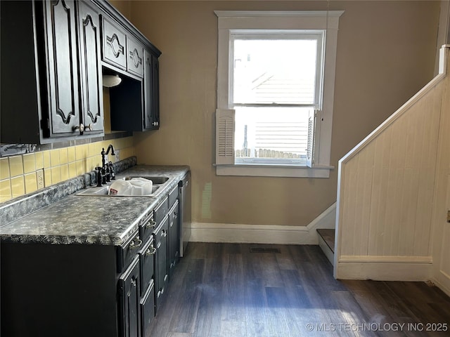 kitchen with dark cabinets, dark wood-style flooring, stainless steel dishwasher, and a sink