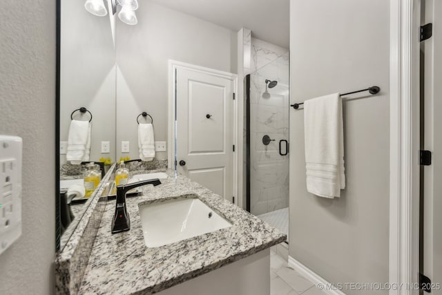 full bath with baseboards, double vanity, a stall shower, marble finish floor, and a sink
