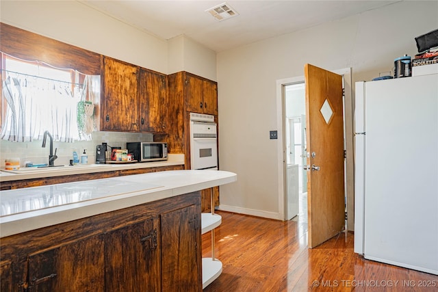 kitchen featuring stainless steel microwave, visible vents, light wood-style flooring, freestanding refrigerator, and a sink