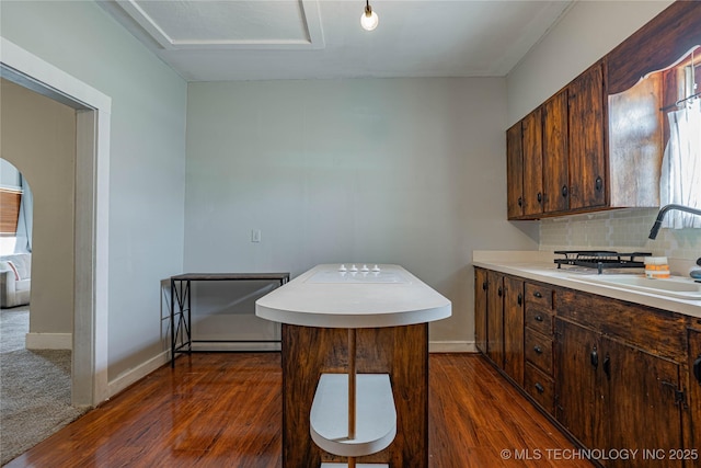 kitchen with a sink, dark wood-type flooring, backsplash, and light countertops