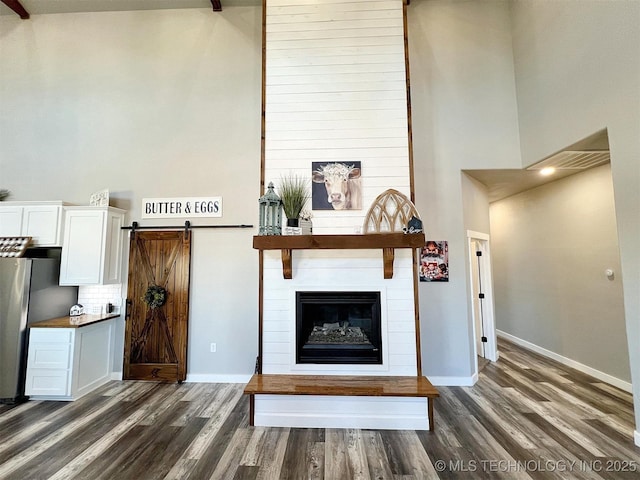 11457 N 510th Rd, Tahlequah, OK 74464 - unfurnished living room featuring dark wood-type flooring, baseboards, a barn door, a high ceiling, and a large fireplace