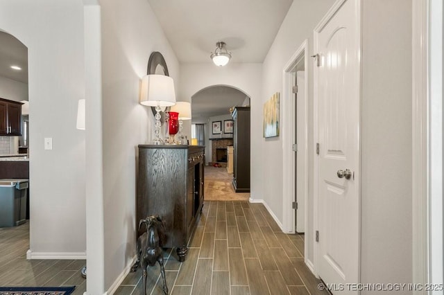 hallway with baseboards, arched walkways, and wood tiled floor
