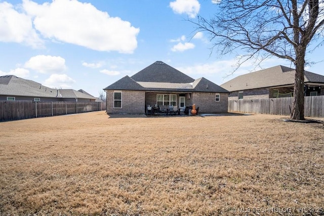 back of house with brick siding, a yard, a patio area, and a fenced backyard