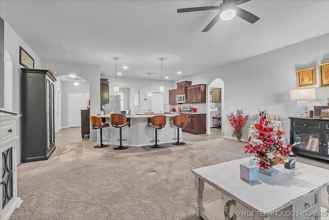 living room featuring ceiling fan, arched walkways, light carpet, baseboards, and recessed lighting