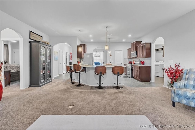 interior space with a kitchen breakfast bar, arched walkways, light carpet, stainless steel appliances, and light countertops