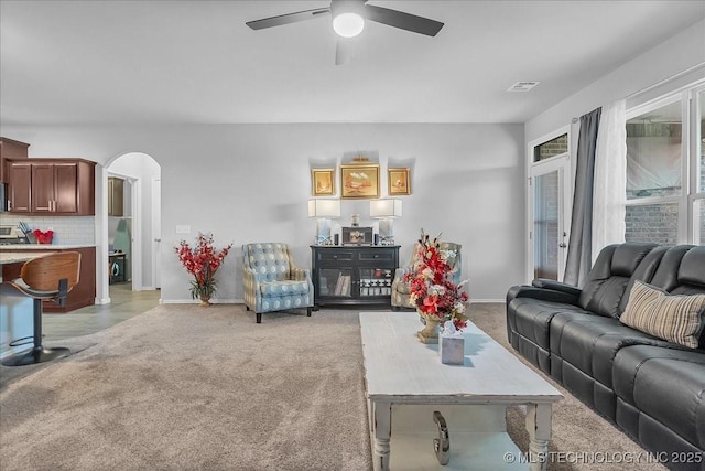 living room with light carpet, a ceiling fan, baseboards, and arched walkways