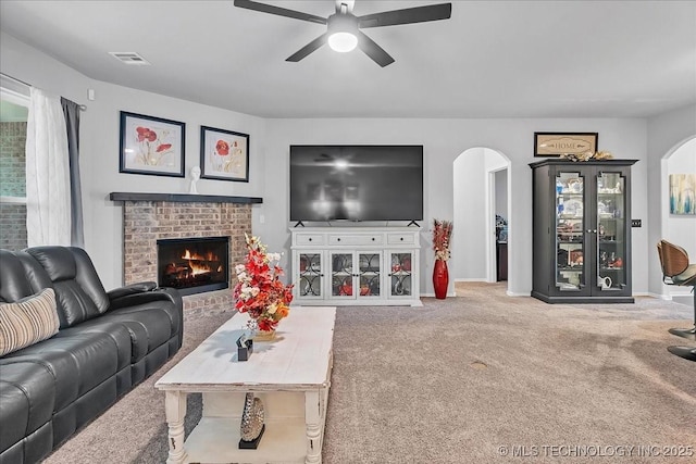 carpeted living area featuring visible vents, arched walkways, baseboards, a fireplace, and ceiling fan