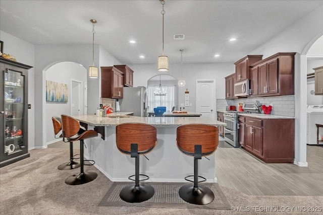 kitchen featuring stainless steel appliances, a breakfast bar, a sink, arched walkways, and washer / dryer