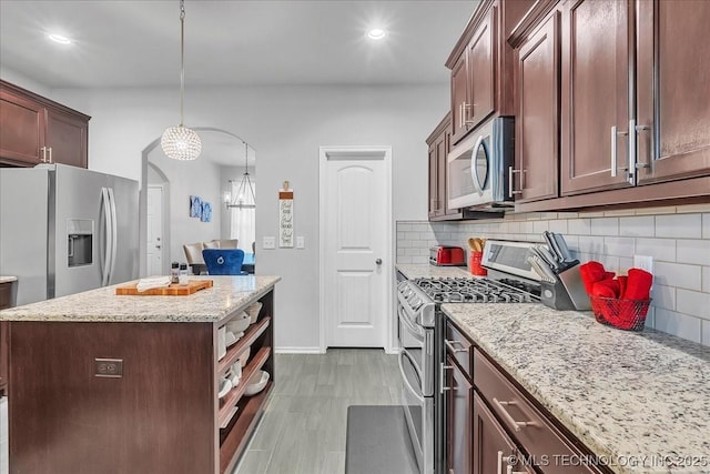 kitchen with tasteful backsplash, stainless steel appliances, baseboards, light stone countertops, and a kitchen island