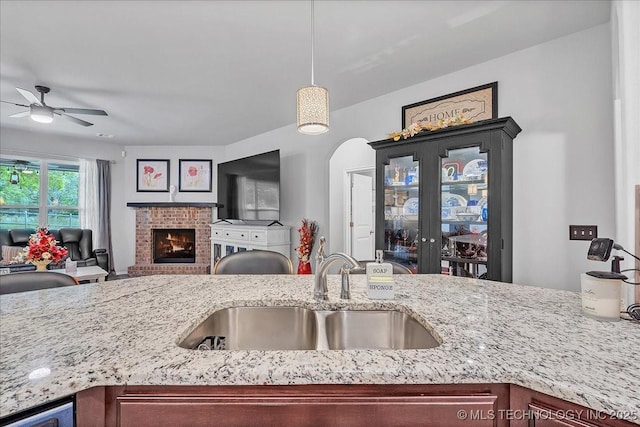 kitchen with a ceiling fan, light stone counters, a sink, open floor plan, and a fireplace
