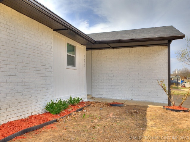 doorway to property with brick siding and a shingled roof