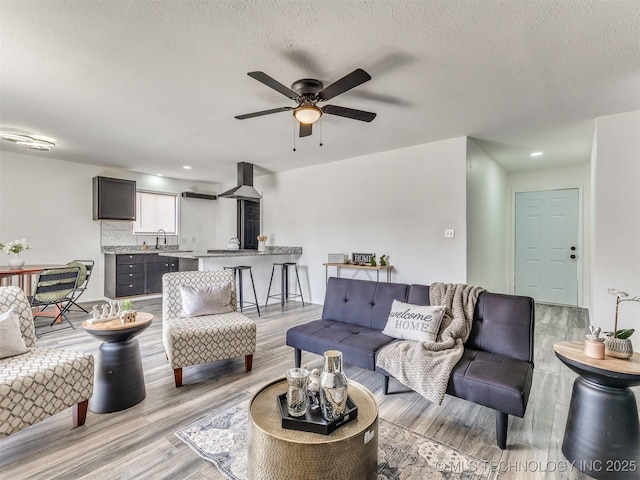 living area featuring light wood-style flooring, a textured ceiling, and a ceiling fan