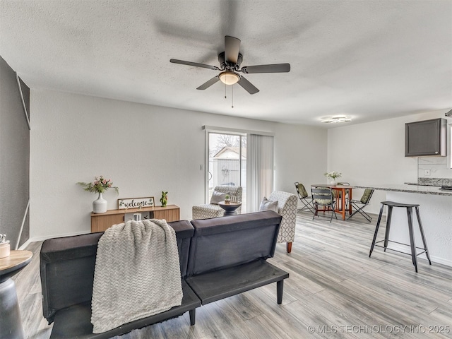 living area with a textured ceiling, light wood-type flooring, and ceiling fan