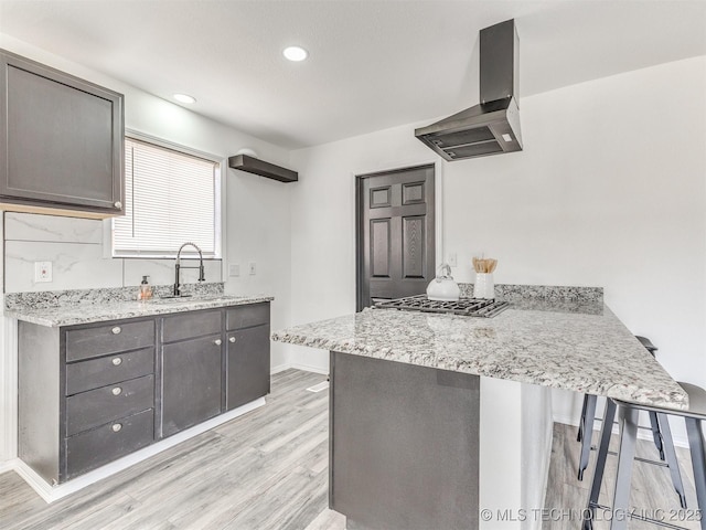 kitchen featuring a peninsula, gray cabinetry, wall chimney exhaust hood, and a sink