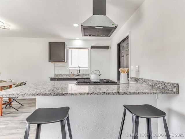 kitchen featuring island exhaust hood, light stone counters, a kitchen breakfast bar, and a peninsula