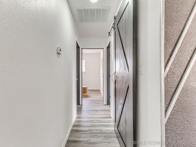 corridor featuring visible vents, light wood finished floors, baseboards, a barn door, and a textured wall