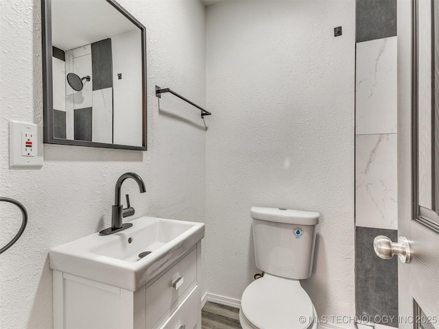 bathroom with wood finished floors, toilet, vanity, and a textured wall