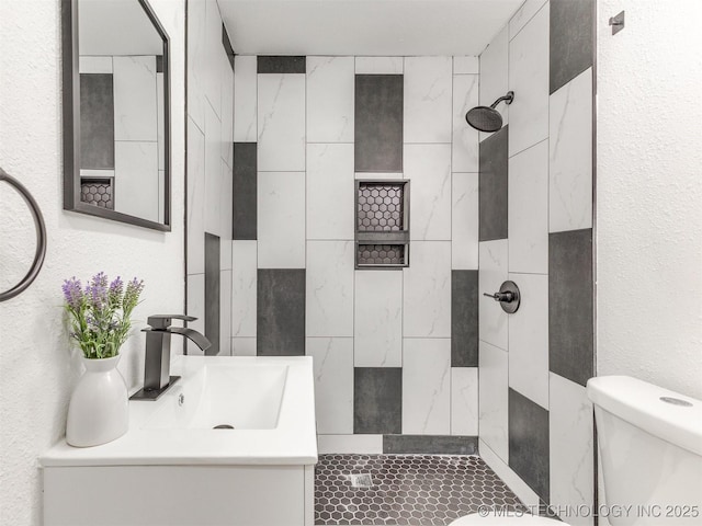 full bathroom with vanity, toilet, a textured wall, and a tile shower
